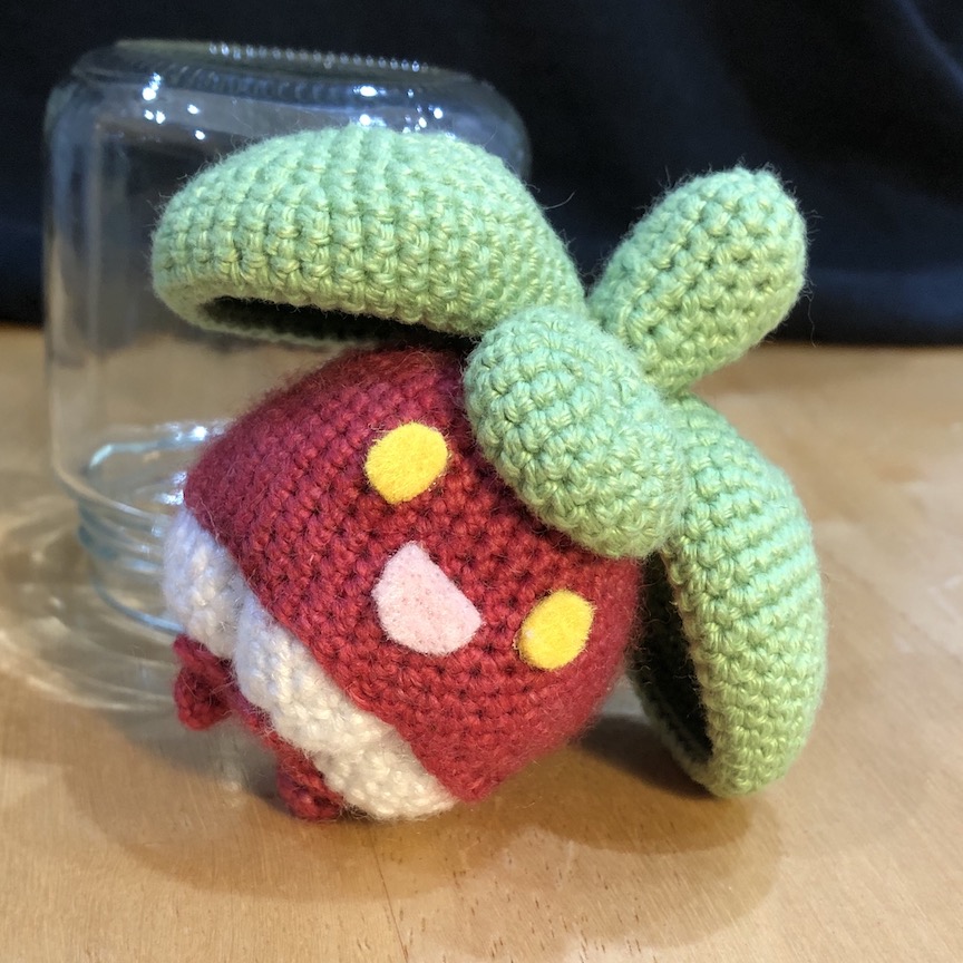 Crocheted bounsweet tilted so that it's leaning on one of it's leaves instead of standing on its feet