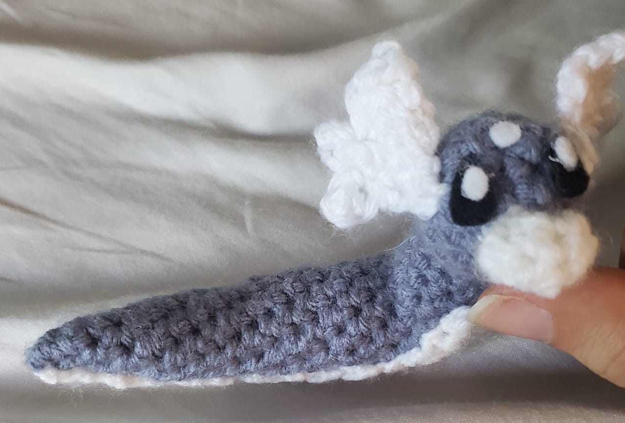 crocheted dratini propped up by a thumb