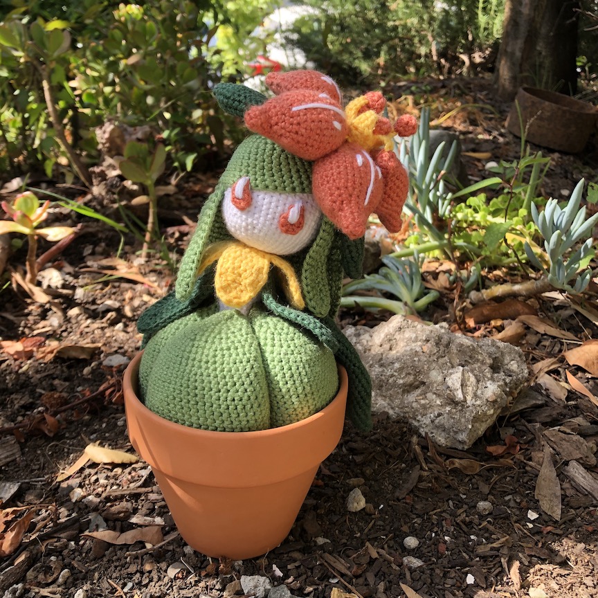 Crocheted lilligant sits in direct sun in a flower pot in a garden