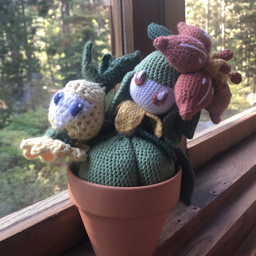 Crocheted lilligant sits in her flower potwith shiny petilil floating next to her