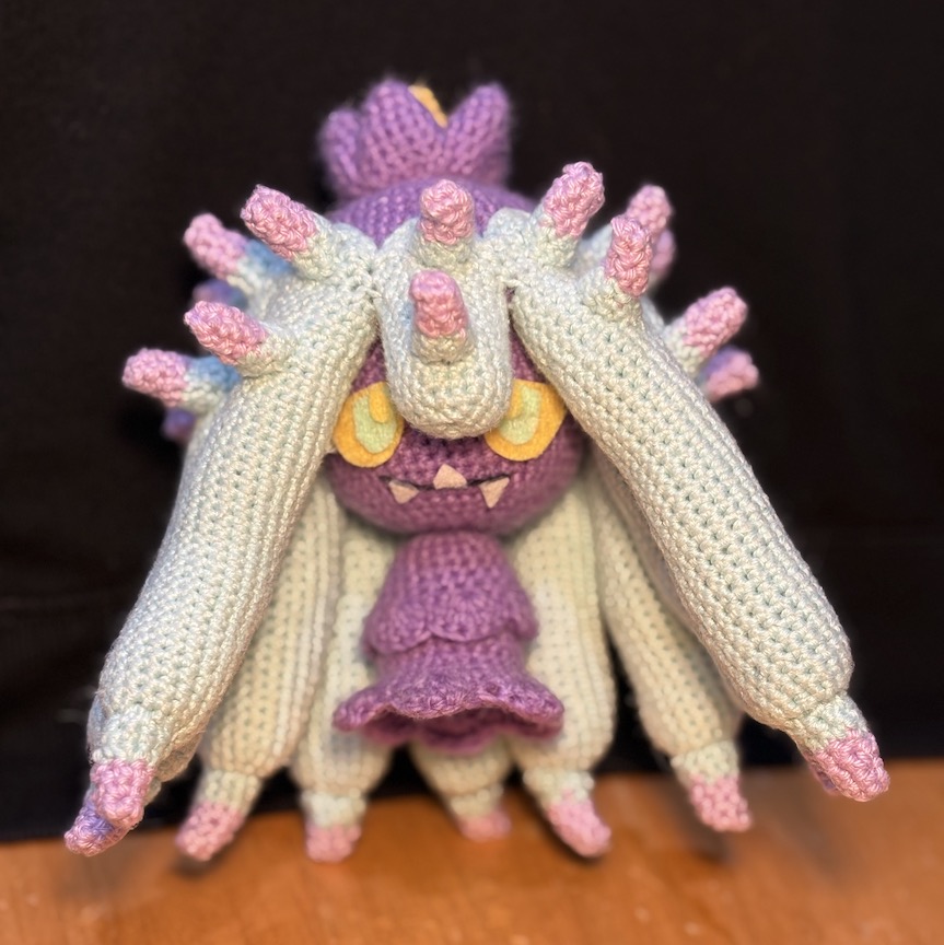 Crocheted mareanie faces towards you, felt eyes looking up at you through hanging tentacles