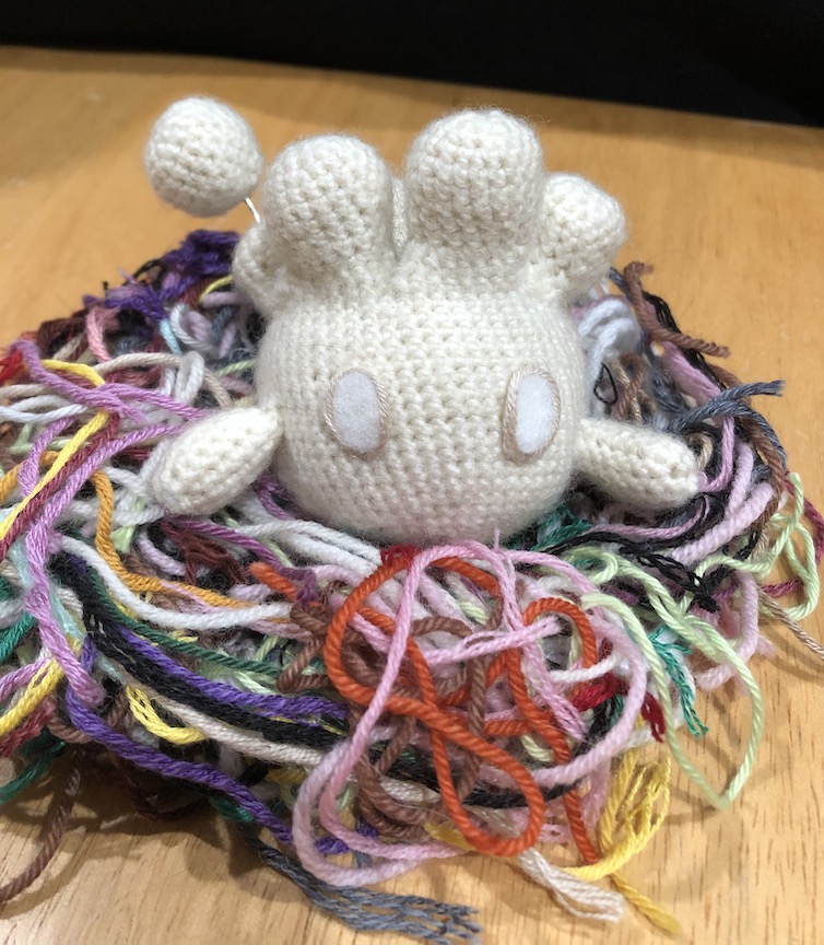 crocheted milcery nestled in a nest of colorful yarn scraps