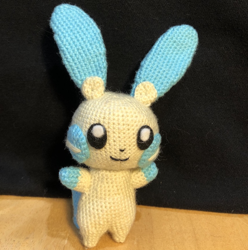 crocheted minun facing head on with a little close mouth smile