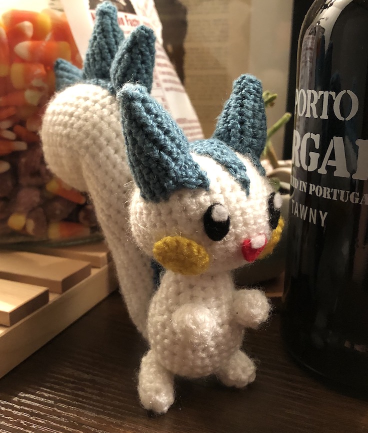 Crocheted pachirisu next to some candy corn and a glass bottle