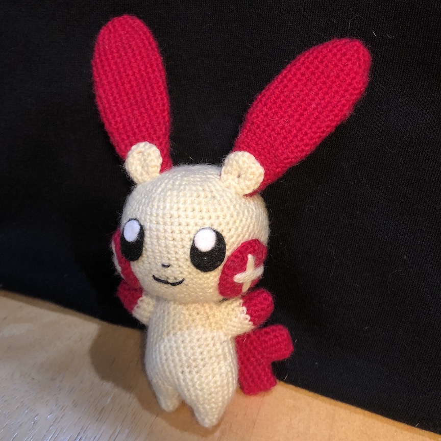 crocheted plusle facing head on with a little close mouth smile