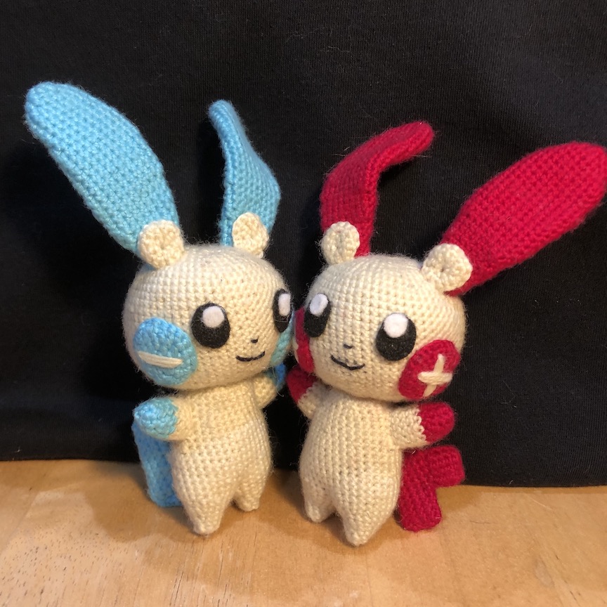 crocheted plusle and minun standing cheek to cheek