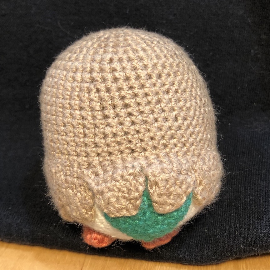 Crochet rowlet facing away from the camera, revealing a green leaf tail