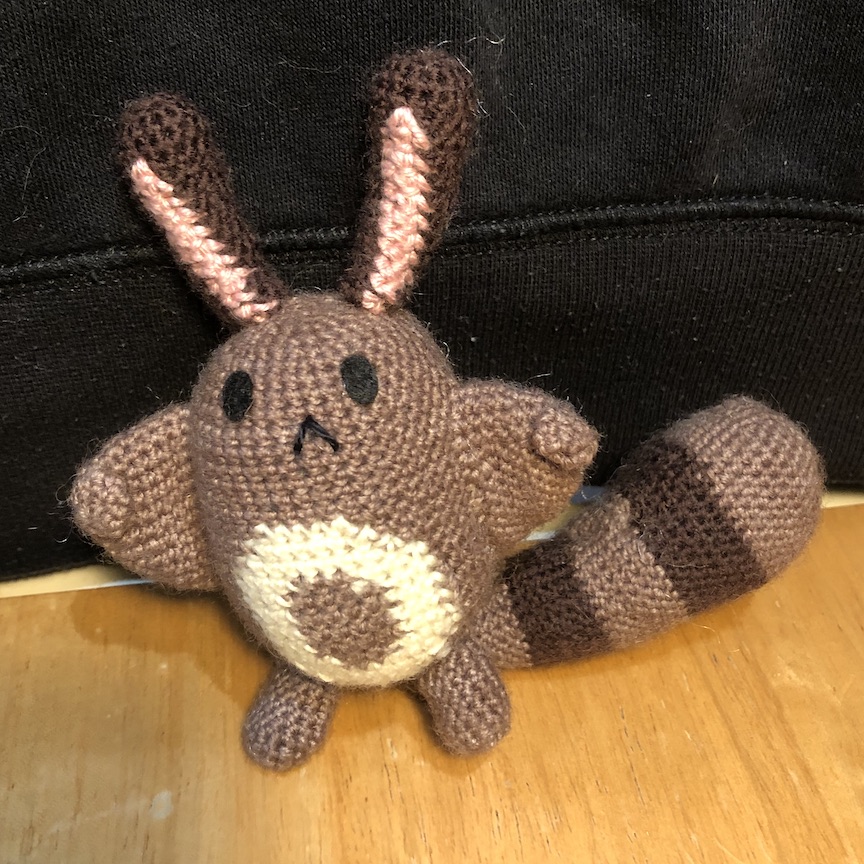 crocheted sentret sitting with his tail off to his right