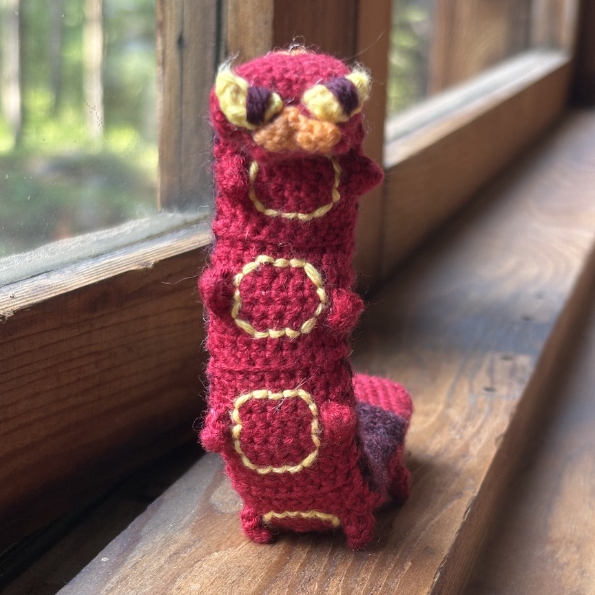 Crocheted sizzlipede standing with most of his belly facing you, showing off his little yellow circles and many tiny feet