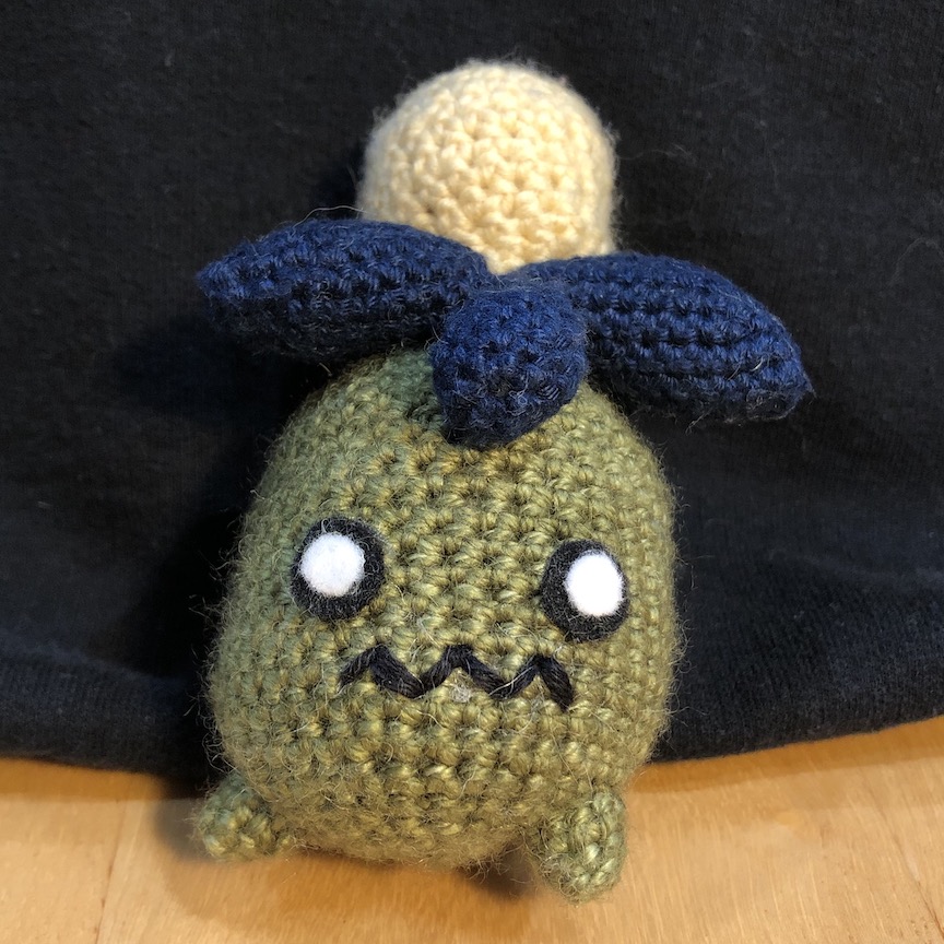 Custom colored crocheted smoliv with an olive grean body, light yellow olive, and navy leaves. The scared mouth is stitched on with black yarn as a zigzag
