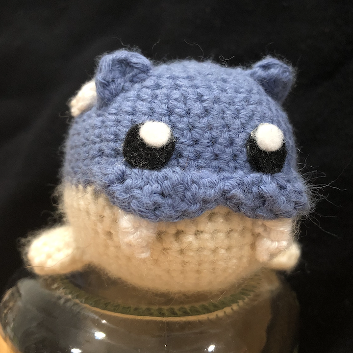 crocheted spheal facing forward, perched on a glass jar