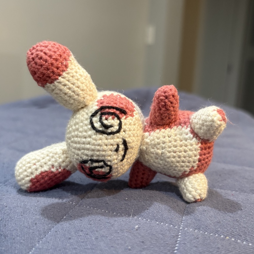 crocheted spinda who has fallen over, but is smiling just the same