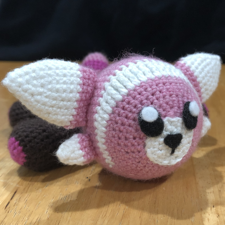 Crocheted stufful laying flat on its belly with all four legs sticking out to the sides