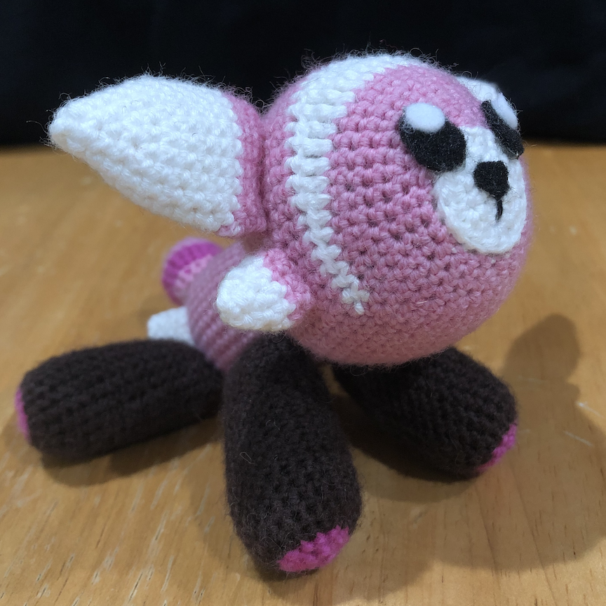 Crocheted stufful sitting with its two front legs propping it up as it looks up at you