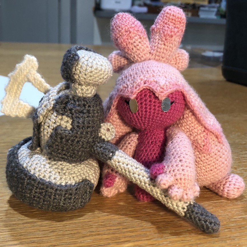 crocheted tinkaton holding her hammer as it rests on the ground. She has shiny reflective silver eyes