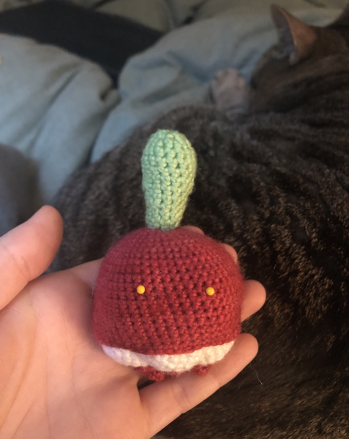 Unfinished crochet bounsweet with yellow pins for eyes and no leaves. He just has the stem and it looks silly