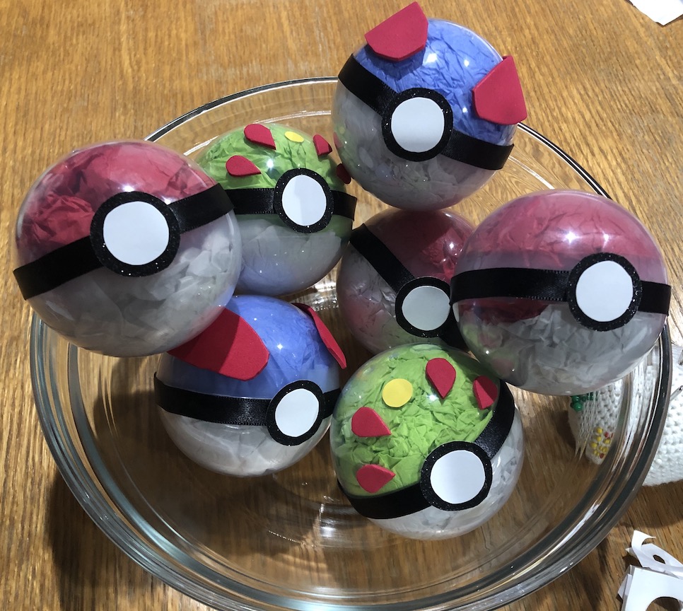 A picture with a bowl of pokéballs made from clear plastic orbs stuffed with colorful tissue paper and with decorations on the outside