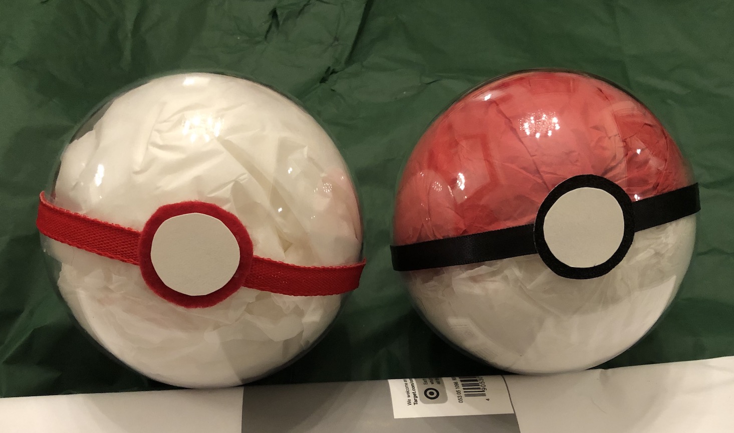 Two clear plastic orbs filled with tissue paper and decorated with ribbon around the middle and cardstock for the buttons. They're a premier ball and a classic pokéball