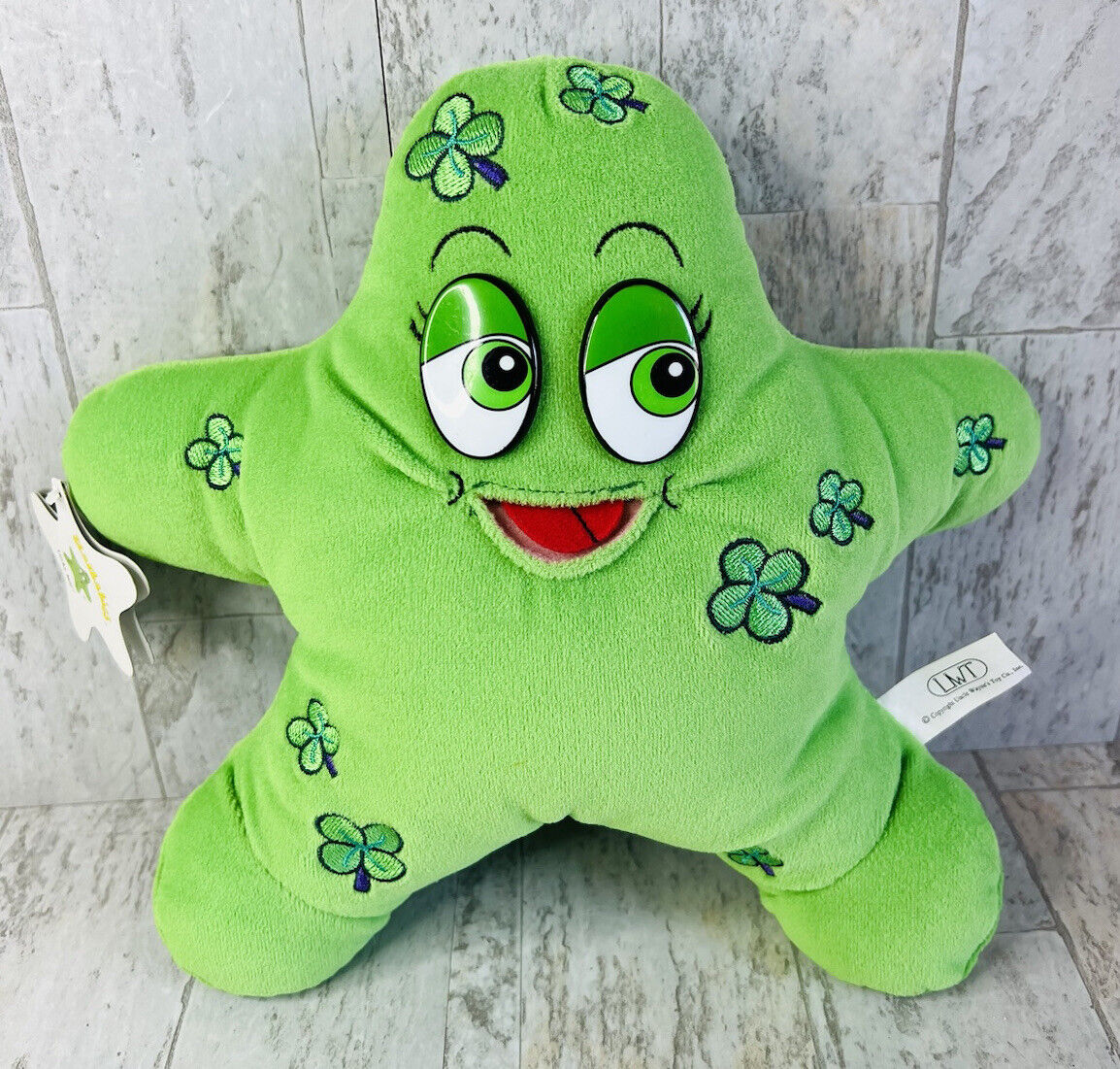 A green star plush with emrboidered four leaf clovers, hard plastic eyes, and an open mouth with a felt tongue. He also has a star shaped tag
